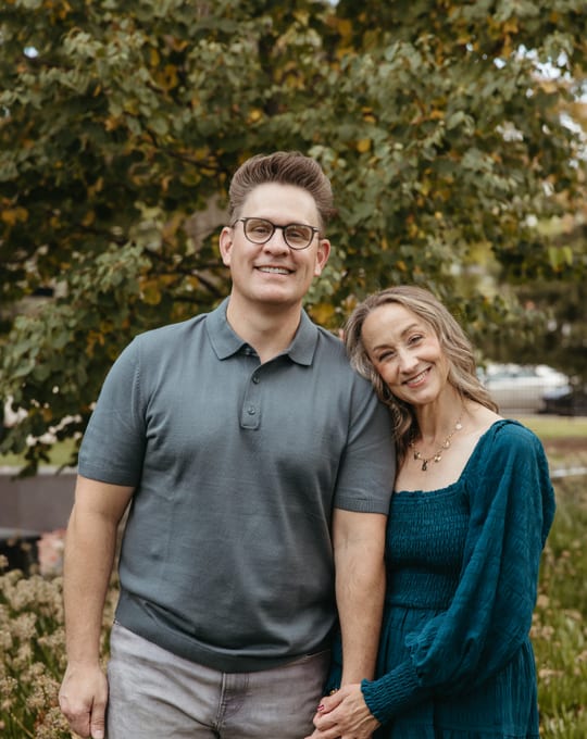 Jason and Jodi Nelson standing together among autumn trees.